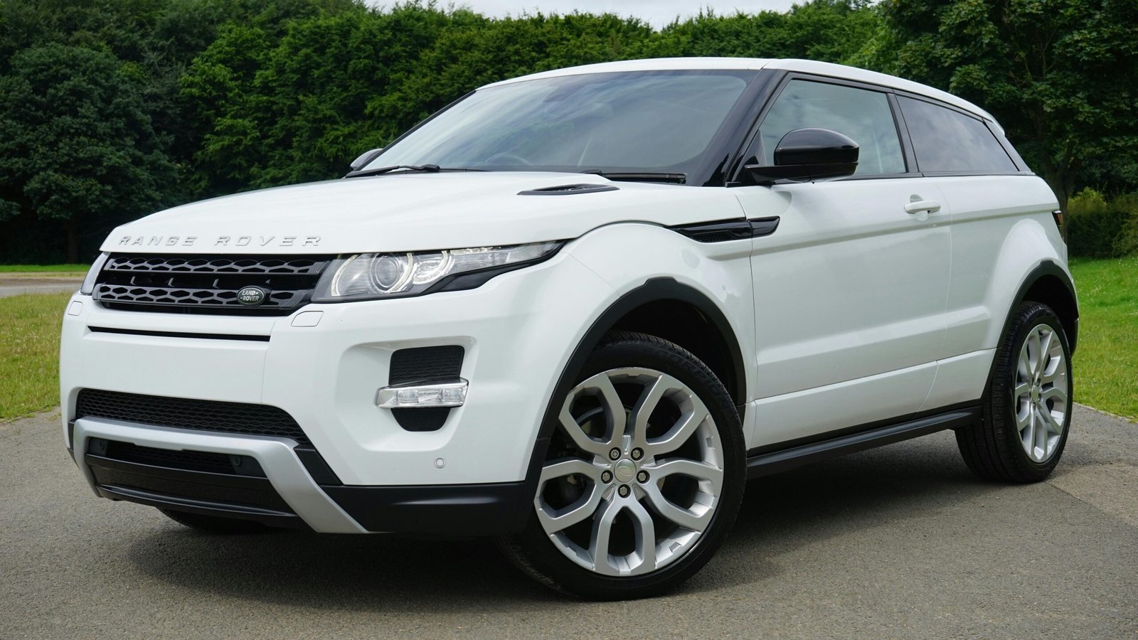 Stylish white Range Rover parked on a road in a green outdoor setting, showcasing its luxury design.